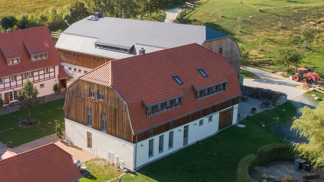 Das Gästehaus des Dreiseithofs mit Holzfassade und rotem Ziegeldach aus der Luft