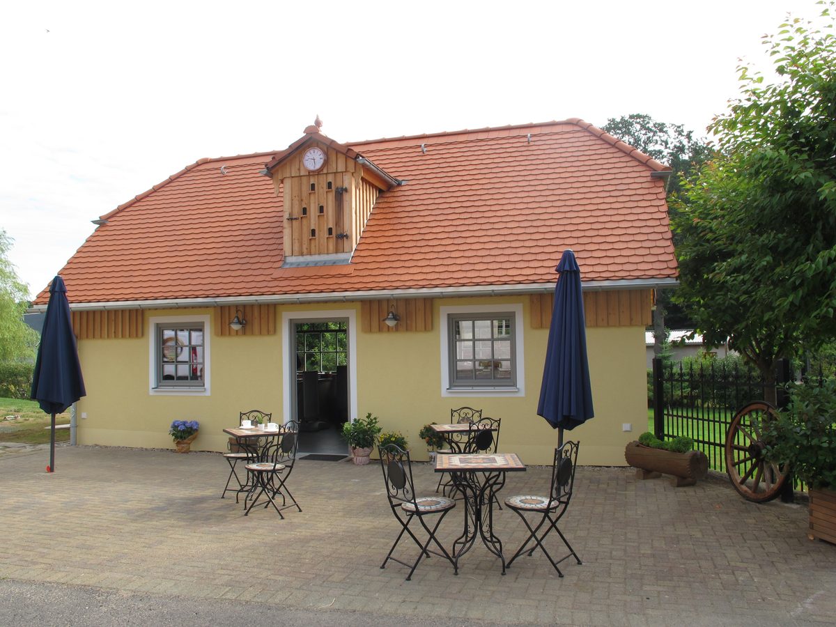 Hofladen des Dreiseithofs, gelbes Nebengebäude mit Terrasse