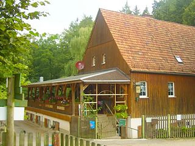 Die Waldgaststätte Höllmühle: holzverkleidetes Mühlengebäude mit Blumenkästen am Waldrand